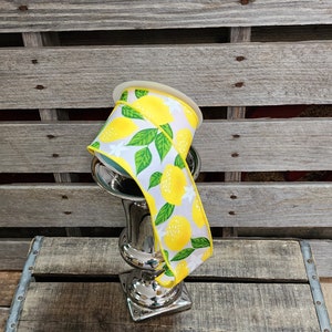 May include: A spool of yellow and white ribbon with a lemon print. The ribbon is wrapped around a silver vase.
