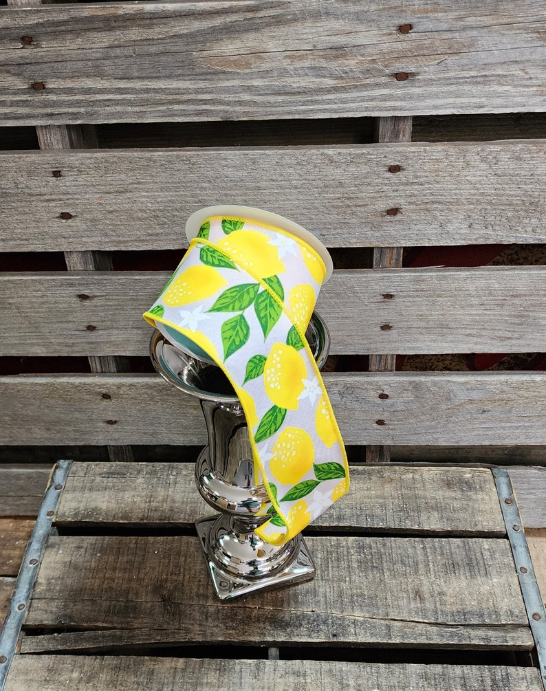 May include: A spool of yellow and white ribbon with a lemon print. The ribbon is wrapped around a silver vase.