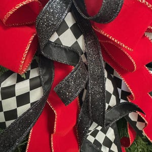 Puede incluir: Primer plano de un lazo decorativo con cinta de terciopelo rojo vibrante con ribete dorado, acentuado por cinta a cuadros en blanco y negro y cinta negra brillante. El lazo es probablemente para la decoraci&oacute;n navide&ntilde;a o de eventos.