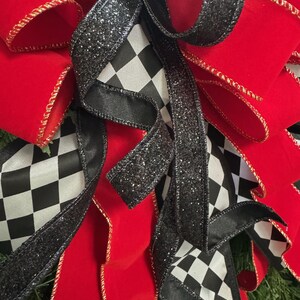 Puede incluir: Primer plano de un lazo decorativo con cinta de terciopelo rojo vibrante con ribete dorado, acentuado por cinta a cuadros en blanco y negro y cinta negra brillante. El lazo es probablemente para la decoraci&oacute;n navide&ntilde;a o de eventos.