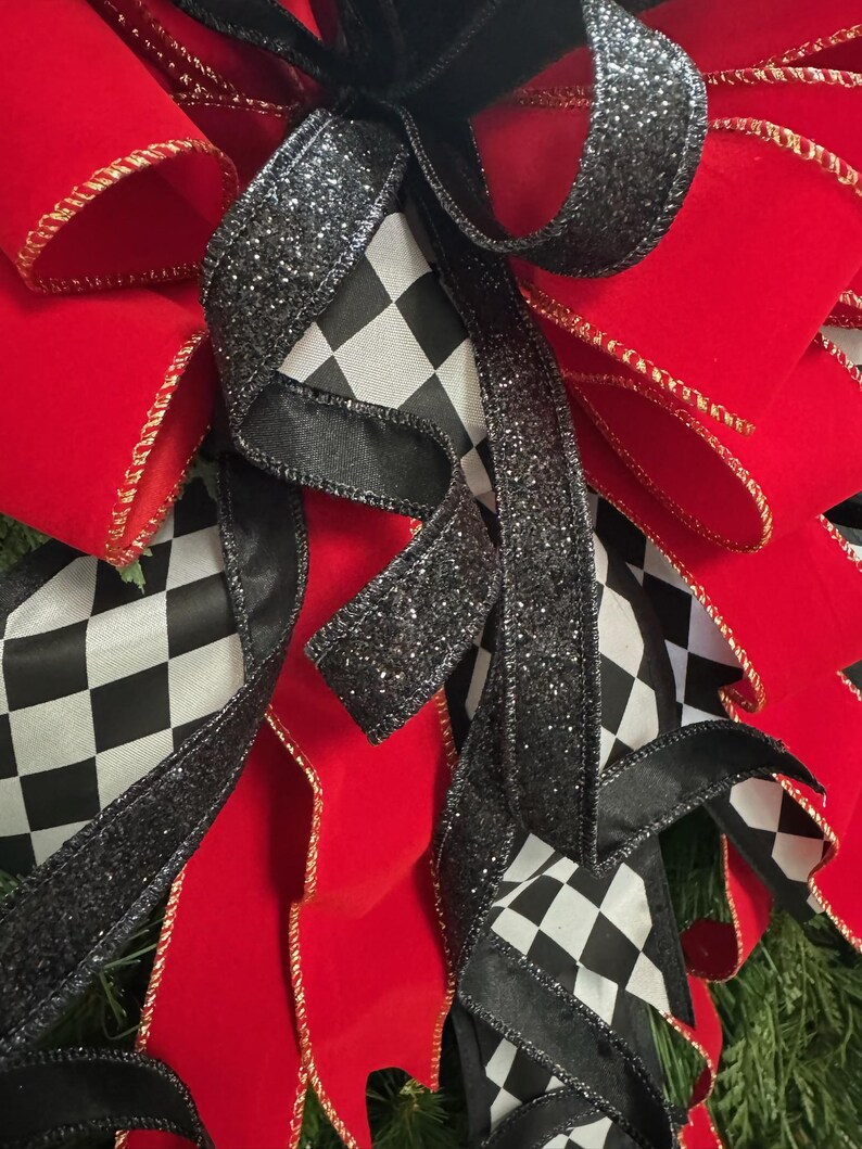 Puede incluir: Primer plano de un lazo decorativo con cinta de terciopelo rojo vibrante con ribete dorado, acentuado por cinta a cuadros en blanco y negro y cinta negra brillante. El lazo es probablemente para la decoraci&oacute;n navide&ntilde;a o de eventos.