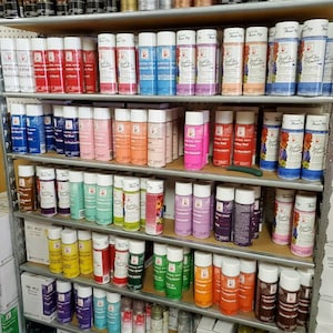 May include: A shelf stocked with rows of spray paint cans in various colors, including silver, gold, red, blue, green, and black. The cans are labeled with the brand name "Just for Flowers" and the words "Glitter Silver" and "Glitter Gold".