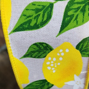 May include: A close-up of a yellow and green fabric ribbon with a lemon print. The ribbon has a white background with yellow lemons and green leaves.