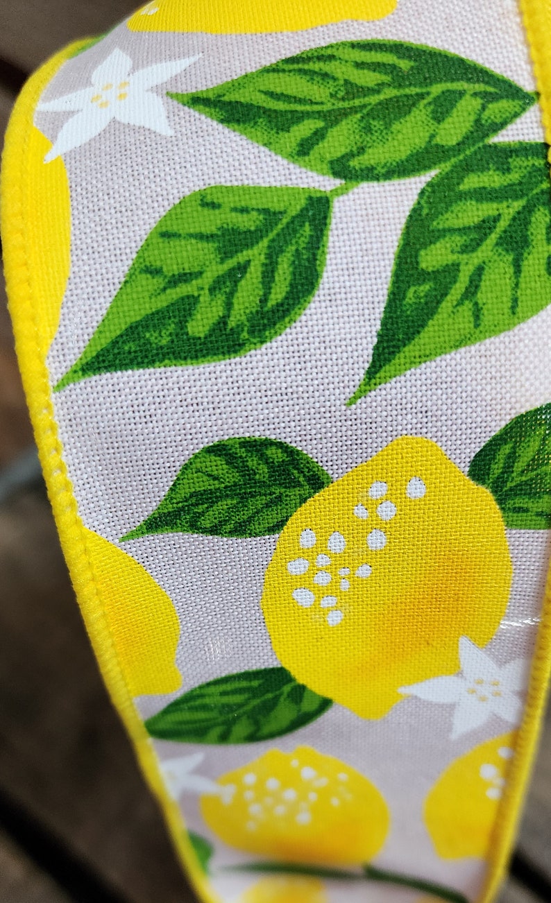 May include: A close-up of a yellow and green fabric ribbon with a lemon print. The ribbon has a white background with yellow lemons and green leaves.