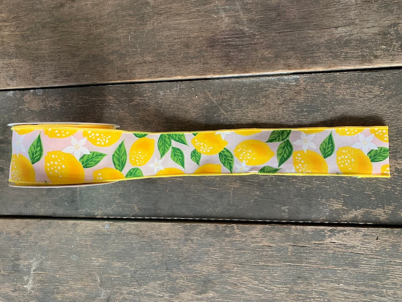 May include: A yellow ribbon with a lemon print. The ribbon has a light pink background with green leaves and white flowers.
