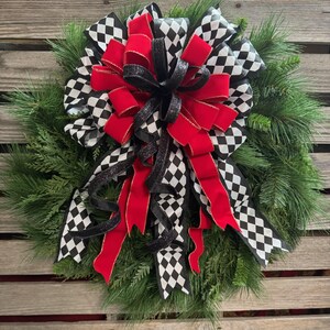 Puede incluir: Una corona festiva con un dise&ntilde;o llamativo. La corona est&aacute; compuesta por follaje de pino verde y un gran lazo. El lazo incorpora cinta a cuadros en blanco y negro, cinta roja brillante y cinta negra brillante.