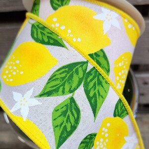 May include: A white ribbon with a yellow lemon print. The ribbon has green leaves and white flowers. The ribbon is edged with a yellow trim.
