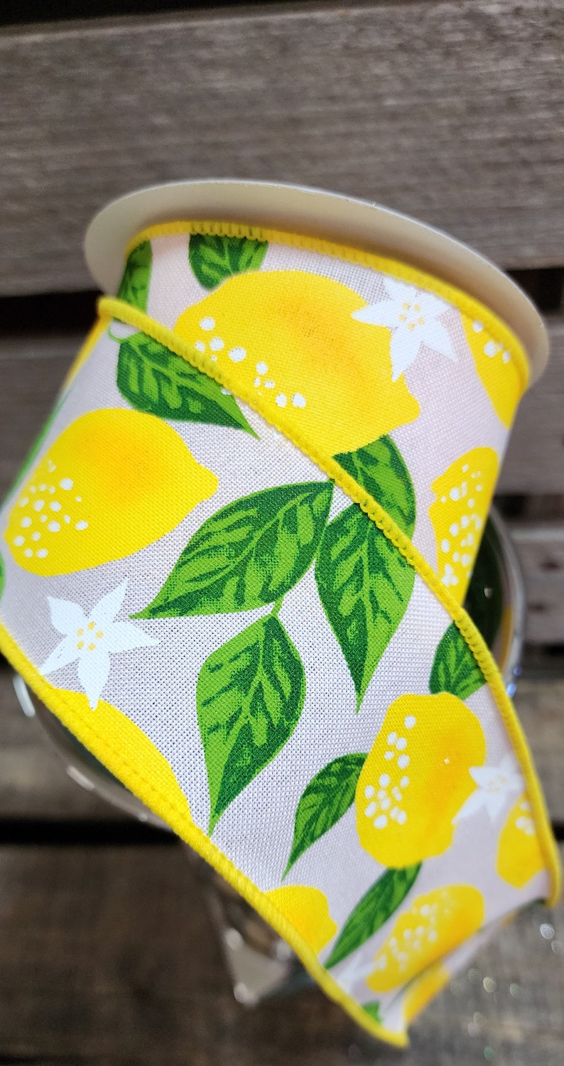 May include: A white ribbon with a yellow lemon print. The ribbon has green leaves and white flowers. The ribbon is edged with a yellow trim.