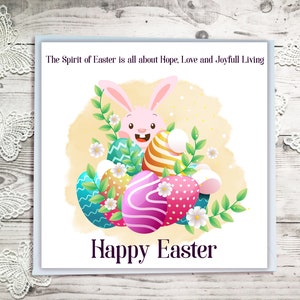 May include: A pink bunny rabbit peeking out from behind a pile of colourful Easter eggs. The eggs are decorated with stripes, polka dots, and swirls. The background is a watercolour wash of yellow and orange. The text "The Spirit of Easter is all about Hope, Love and Joyful Living" is at the top of the card. The text "Happy Easter" is at the bottom of the card.