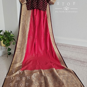 May include: A vibrant pink saree with a maroon border and gold accents. The saree features a detailed geometric pattern along the border and a matching maroon blouse with white polka dots. The text "VAVS WOMENS STOP" is visible.