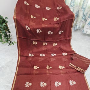 May include: A maroon fabric with gold embroidery featuring floral patterns. The fabric has a gold border and a matching folded piece. The embroidery is evenly spaced across the fabric.