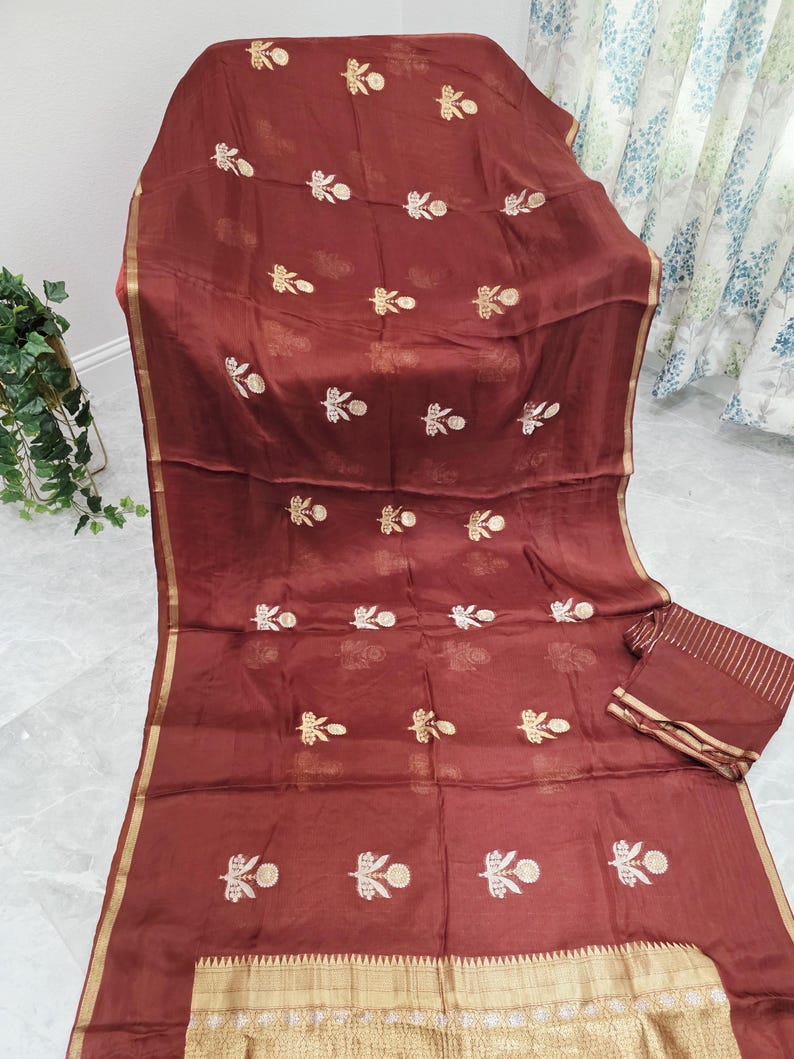 May include: A maroon fabric with gold embroidery featuring floral patterns. The fabric has a gold border and a matching folded piece. The embroidery is evenly spaced across the fabric.