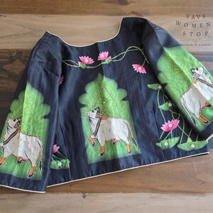 Op de afbeelding: Zwarte blouse met een uniek ontwerp met witte koeien met oranje hoeven, tegen groene en roze bloemaccenten. De blouse heeft een ronde hals en korte mouwen. De tekst "VAVS WOMENS STOP" is zichtbaar.