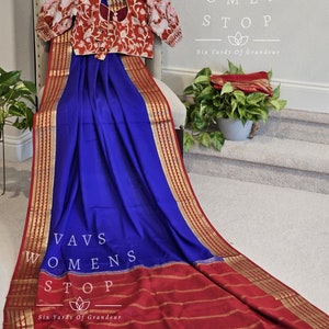 May include: A blue and red saree with gold trim. The saree is draped over a chair and has a red blouse with gold embroidery. The text "Vavs Womens Stop Six Yards Of Grandeur" is visible on the image.