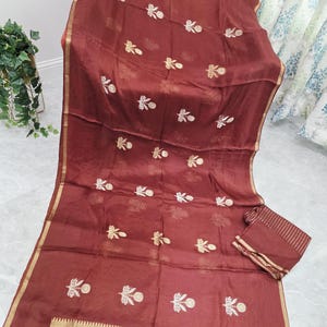 May include: A maroon fabric with gold trim and embroidered floral patterns. The fabric is draped, showcasing the intricate design and texture. A matching rectangular piece is also visible.