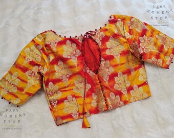 Puede incluir: Una blusa vibrante y estampada en tonos amarillos, naranjas y rojos. La tela presenta un diseño floral con detalles dorados. La blusa tiene mangas tres cuartos y un escote de ojo de cerradura. El texto "VAVS WOMENS STOP" es visible.