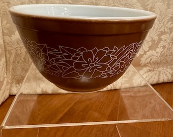 May include: A brown mixing bowl with a white floral design. The bowl is sitting on a clear acrylic stand.
