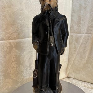 May include: A black ceramic bottle shaped like a man wearing a black hat and holding a rifle. The bottle is labeled "Devil Anse Hatfield" and "Beam 1795 Bourbon Whiskey".