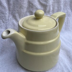 May include: A pale yellow ceramic teapot with a lid and a handle. The teapot has a rounded body and a spout.