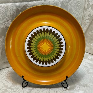 May include: A vintage orange and white serving tray with a circular design featuring green, brown, and yellow concentric circles. The tray has a raised center section with a similar design.