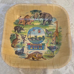 May include: A square, woven, wooden tray with a colorful illustration of animals from the San Diego Zoo. The tray features a tiger, giraffe, ostrich, zebra, elephant, lion, monkey, kangaroo, seal, and a rhinoceros. The text "San Diego Zoo" is printed in the center of the tray.