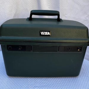 May include: Dark green rectangular carrying case with a black handle on top. The case has a rectangular vent and the word "VISA" in white letters. The case has two black latches on the front.