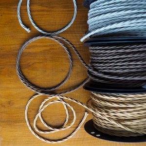 May include: Spools of twisted electrical wire in shades of grey, brown, and beige. The wire is arranged in circles on a wooden surface. The spools are black. The image shows a variety of colours and textures.