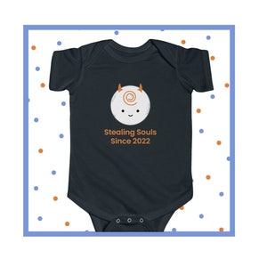 May include: Dark navy blue baby bodysuit with a cartoon graphic of a smiling white creature with horns and a swirl design. The text "Stealing Souls Since 2022" is printed below the graphic. The bodysuit is a one-piece garment.