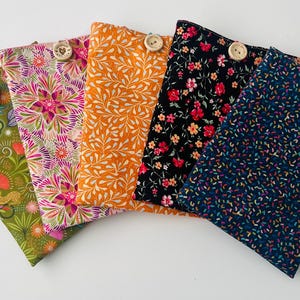 May include: Five rectangular fabric pouches arranged in a fan shape. Each pouch features a unique pattern including green jungle, pink floral, orange leaf, black floral, and navy confetti prints. Each pouch is secured with a round wooden button.