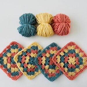 May include: Four crocheted granny squares in teal, yellow, and coral colors. The squares are joined together to form a larger piece.