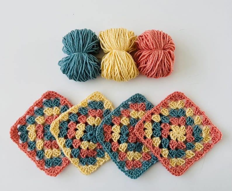 May include: Four crocheted granny squares in teal, yellow, and coral colors. The squares are joined together to form a larger piece.