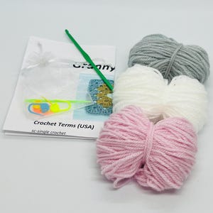 May include: A crochet kit with three balls of yarn in pink, white, and gray, a crochet hook, and instructions. The instructions include the term "sc-single crochet".