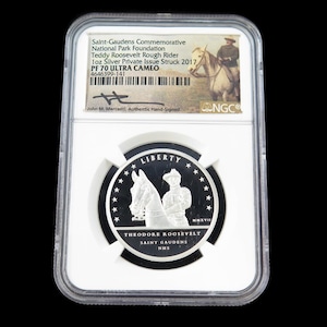 Peut inclure: Une pièce de monnaie en argent représentant Theodore Roosevelt à cheval, dans un étui de protection transparent. La pièce porte l'inscription "LIBERTY" et le texte "THEODORE ROOSEVELT SAINT GAUDENS." L'étui indique "1oz Silver Private Issue Struck 2017."