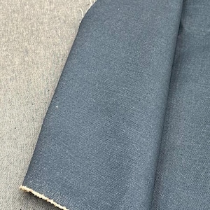 May include: A piece of folded fabric featuring a dual-sided design with a dark blue, smooth-textured side and a lighter, heathered gray side. The material shows a visible weave pattern and raw, frayed edges along the folded section of the textile.
