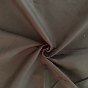 May include: Black fabric with a smooth, silky texture. The fabric is folded and draped, showing its soft, flowing quality.