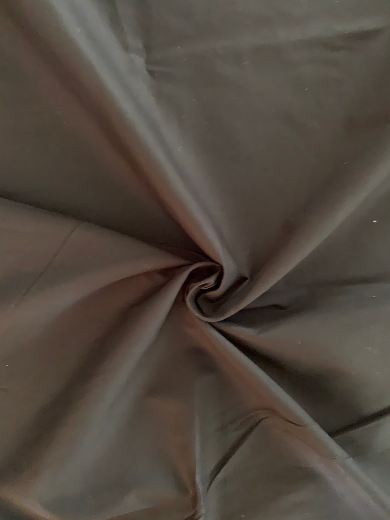 May include: Black fabric with a smooth, silky texture. The fabric is folded and draped, showing its soft, flowing quality.