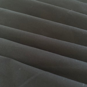 May include: Close-up of black fabric folded in a series of pleats. The fabric has a smooth, slightly textured surface.