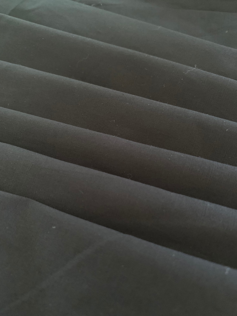 May include: Close-up of black fabric folded in a series of pleats. The fabric has a smooth, slightly textured surface.