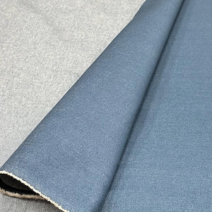 May include: A folded piece of fabric featuring a deep blue side with a smooth, matte texture and a contrasting light gray, heathered underside. The material displays a visible woven grain and a raw, frayed edge along the diagonal fold line.