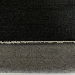 May include: Black denim fabric with a raw edge. The fabric has a subtle texture and a slightly faded appearance.