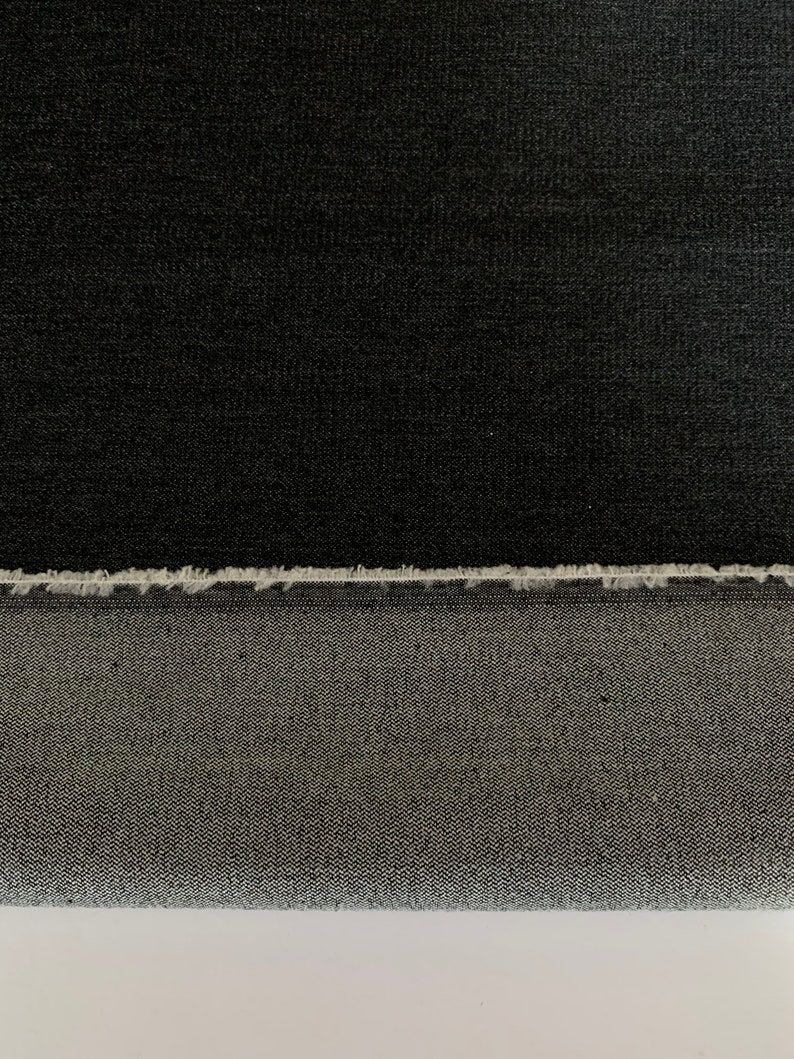 May include: Black denim fabric with a raw edge. The fabric has a subtle texture and a slightly faded appearance.