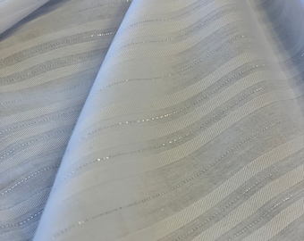 May include: White sheer fabric with silver stripes. The fabric is folded and draped, showing the texture and sheen of the silver stripes.