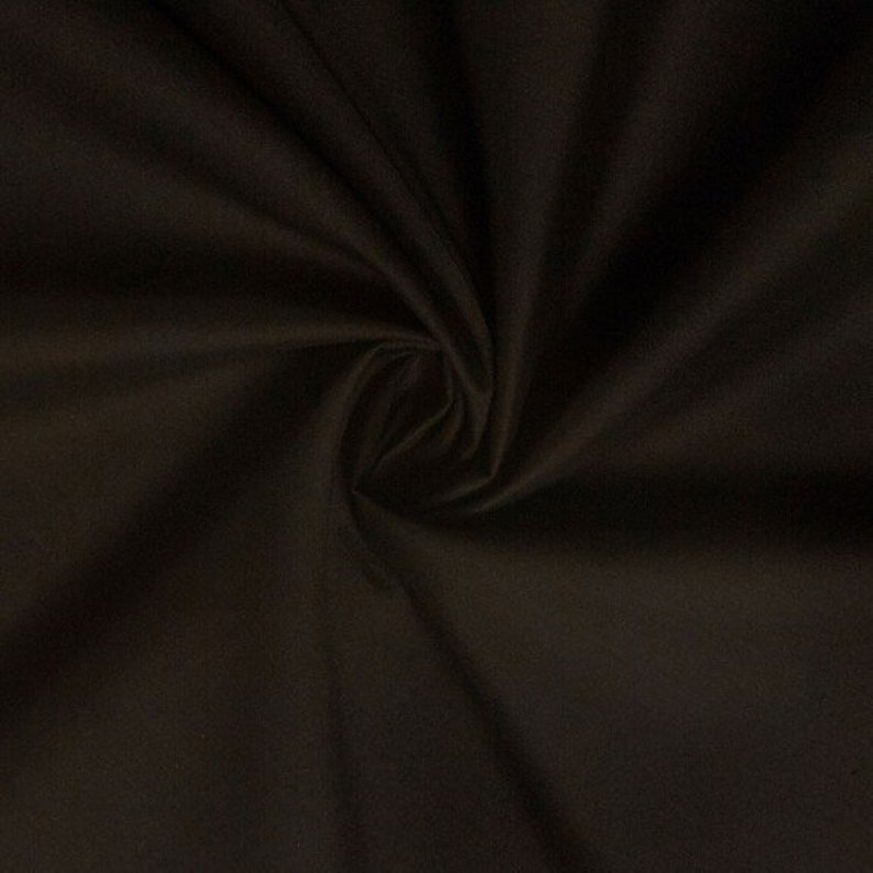 May include: A close-up of a dark brown fabric with a smooth texture. The fabric is folded and draped, showing its soft and pliable nature.