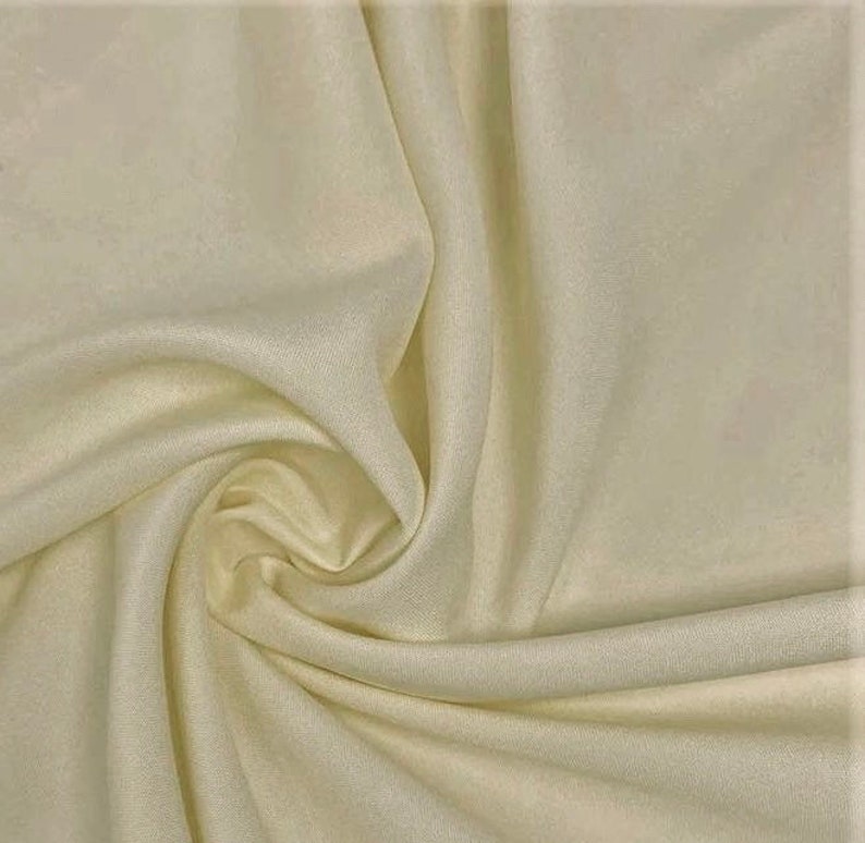 May include: Cream colored fabric with a smooth texture. The fabric is draped and folded, showing its soft and flowing nature.