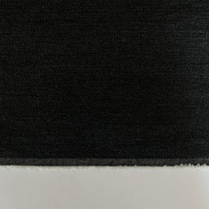 May include: A close-up of a black fabric with a textured surface. The fabric has a raw edge.