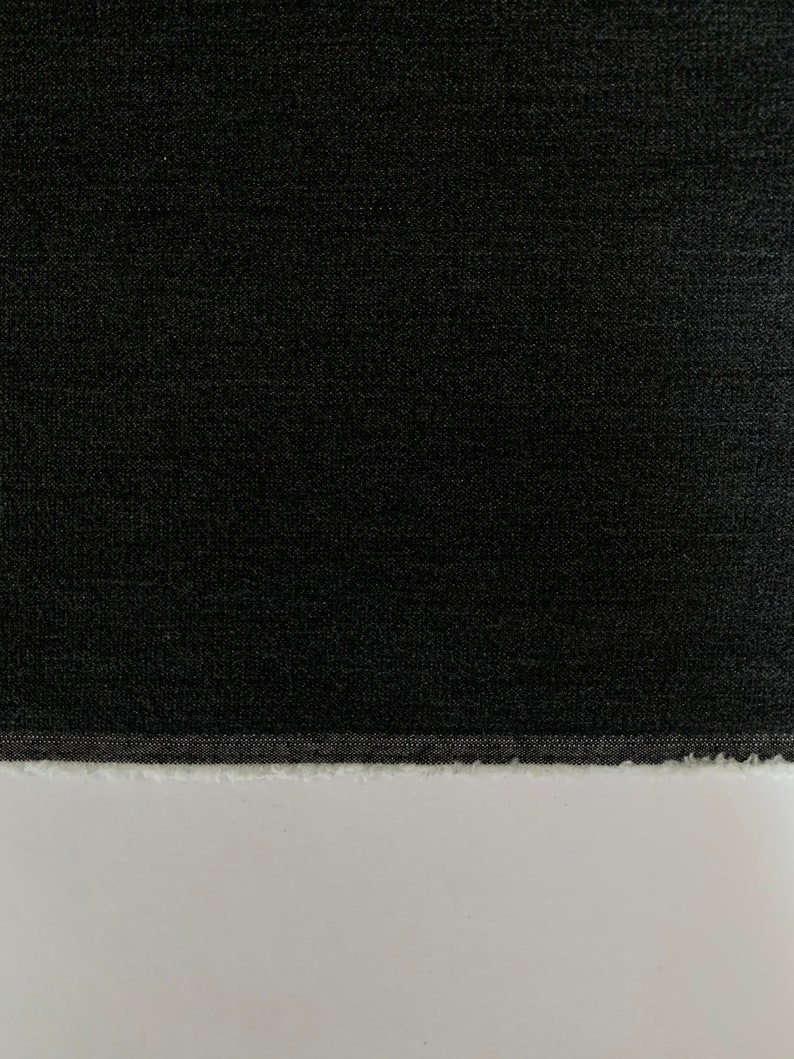 May include: A close-up of a black fabric with a textured surface. The fabric has a raw edge.