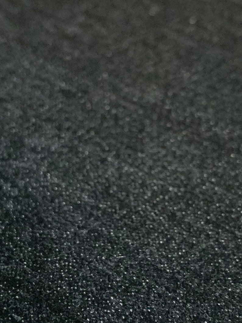 May include: Close-up of a black textured fabric with a subtle sheen. The fabric has a fine, almost granular texture.