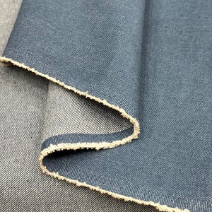 May include: A piece of dark blue denim fabric with a visible twill weave pattern. The material is folded over to reveal a lighter, off-white underside with a raw, frayed edge along the fold, showcasing the contrast between the two sides.