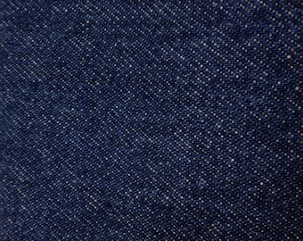May include: Close-up of a dark blue denim fabric with a diagonal weave pattern. The fabric has a subtle white fleck throughout.