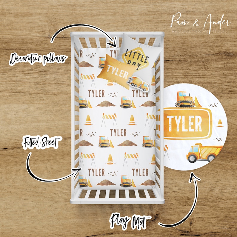 May include: A white crib with a fitted sheet and a decorative pillow with a construction theme. The sheet has a pattern of yellow construction vehicles, cones, and barriers. The pillow has the words "Little Boy" and "Tyler" on it. There is also a round play mat with a yellow construction truck and the name "Tyler" on it.